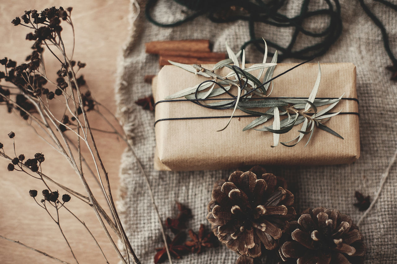 Merry Christmas concept, rustic atmospheric flat lay. Stylish gift box with green branch and fir branches, anise, pine cones, cinnamon on rustic wooden background. Simple eco wrapped present