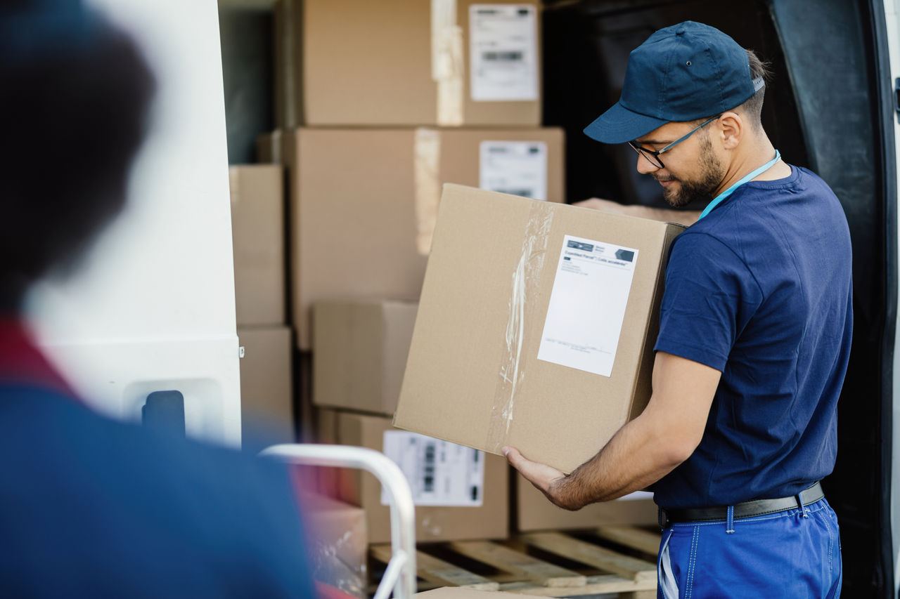 Young manual worker preparing packages for shipment and carrying boxes in a delivery van. 