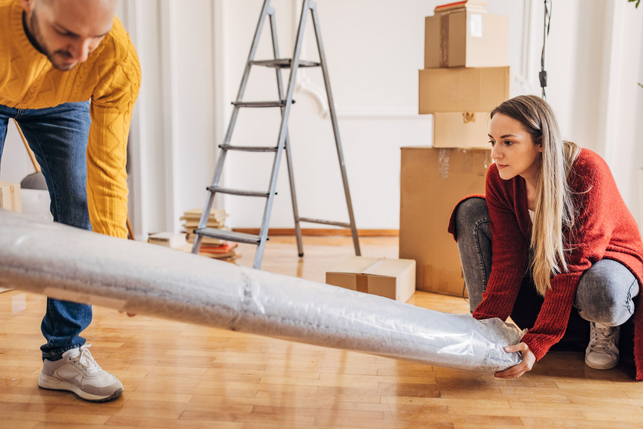 Man and woman, young couple carrying carpet in their new home.