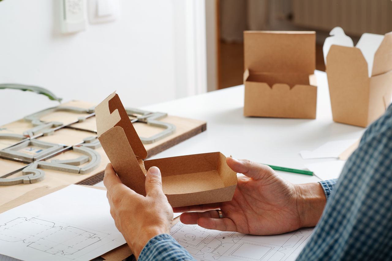 Male hands holding a box in hands, thinking process on ways to improve it. Sitting behind the desk. No face.