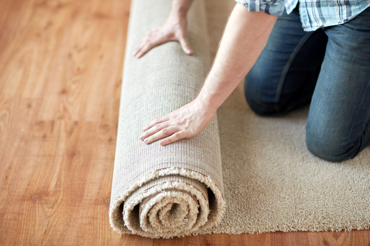 repair, building and home concept - close up of male hands rolling carpet